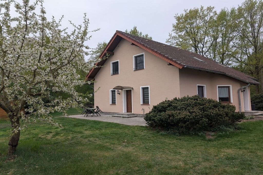 Ein zweigeschossiges Haus mit einem geneigten Dach, einer Veranda und einem kleinen Vorgarten mit Rasen und einem Baum mit weißen Blüten.