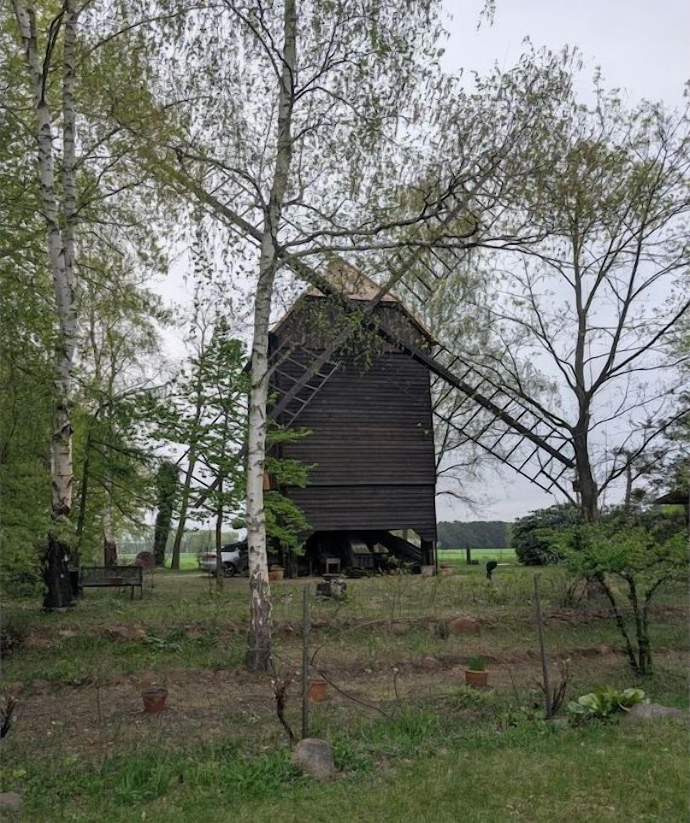 A rustic barn structure surrounded by trees and open fields.