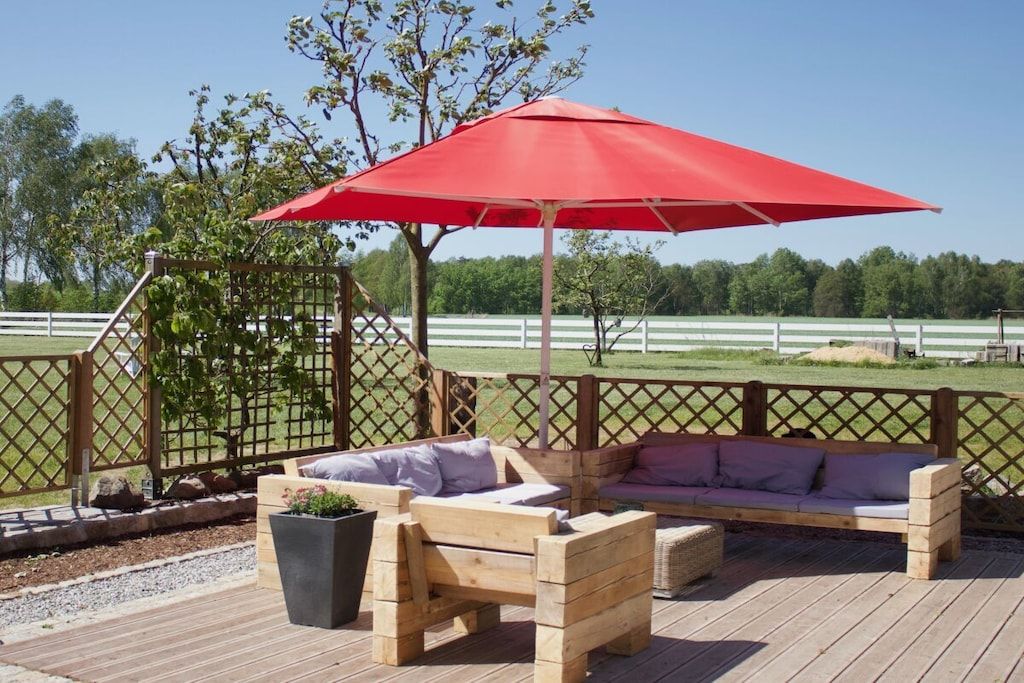 Una terraza de madera con un paraguas rojo, bancos de madera y un cerramiento de celosía.