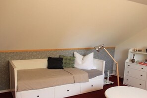 A bedroom with a bed, bedside table, lamp, and a small white dresser. - MAJA The Spree Garden (Cottbus)