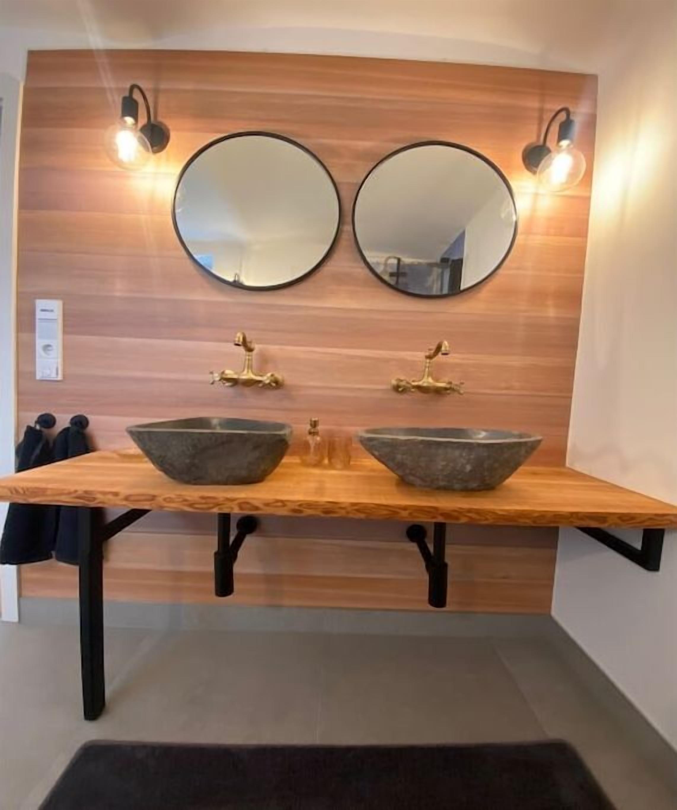 Une salle de bain avec deux miroirs ronds, un meuble-lavabo en bois et un tapis noir.