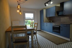 A compact kitchen with a dining table and chairs, a stove, and cabinets. - Holiday apartment with 2 bedrooms (Friedrichskoog)