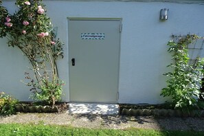 A white door with a sign reading 'Fahradgarage' and a small garden with potted plants and a climbing vine. - Holiday apartment with 2 bedrooms (Friedrichskoog)