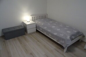 Ein kleines Zimmer mit einem Einzelbett, einem Nachttisch, einer Nachttischlampe und einer Sitzbank.