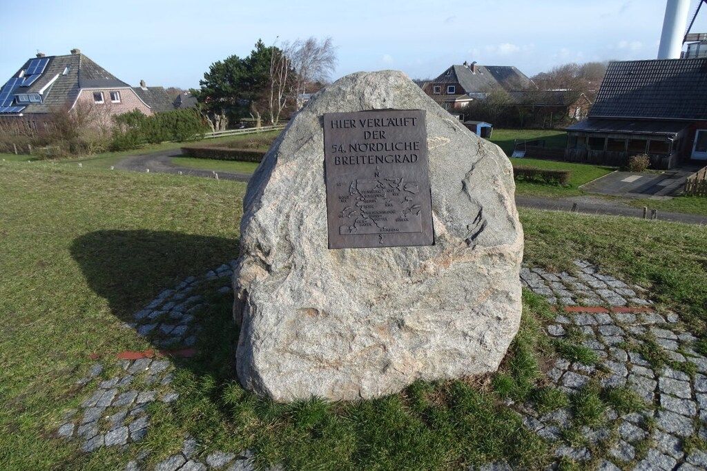 Un monumento in pietra con una targa in una zona erbosa, con case sullo sfondo.