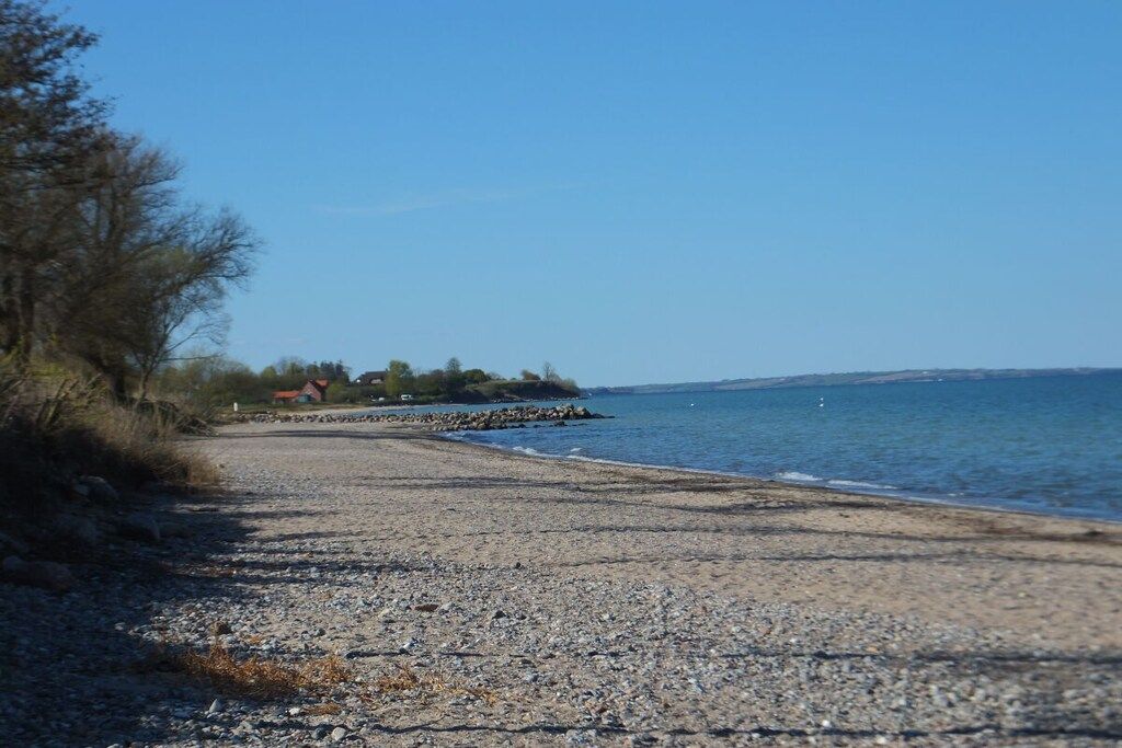 A pebbled beach with a clear sky, a distant shoreline, and a small building.