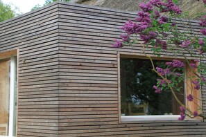 A modern wooden cabin with a large window and a blooming purple flower bush. - Ini's Kate West berth (Usedom)