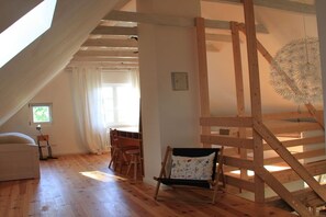Une pièce avec un plafond en pente, un plancher en bois, un lit, une chaise, une table et un luminaire suspendu.