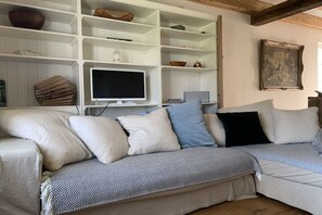 Un salon avec un canapé blanc, un téléviseur posé sur un meuble et une bibliothèque contenant divers objets.