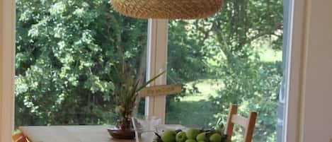 Uma mesa de jantar de madeira com cadeiras, uma luminária pendente de palha e uma cesta de frutas.