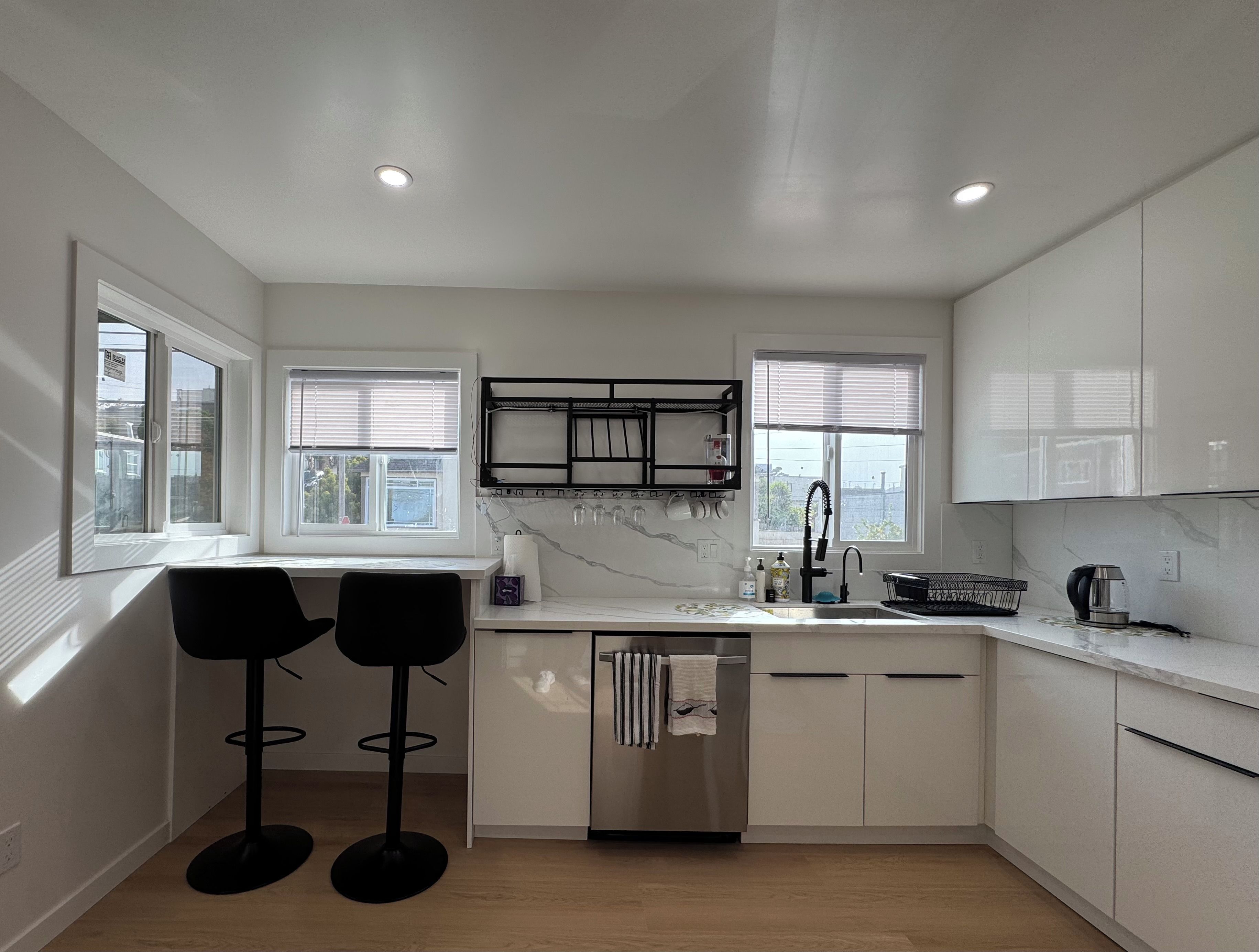 A modern kitchen with white cabinets, a stainless steel dishwasher, and a black bar stool.