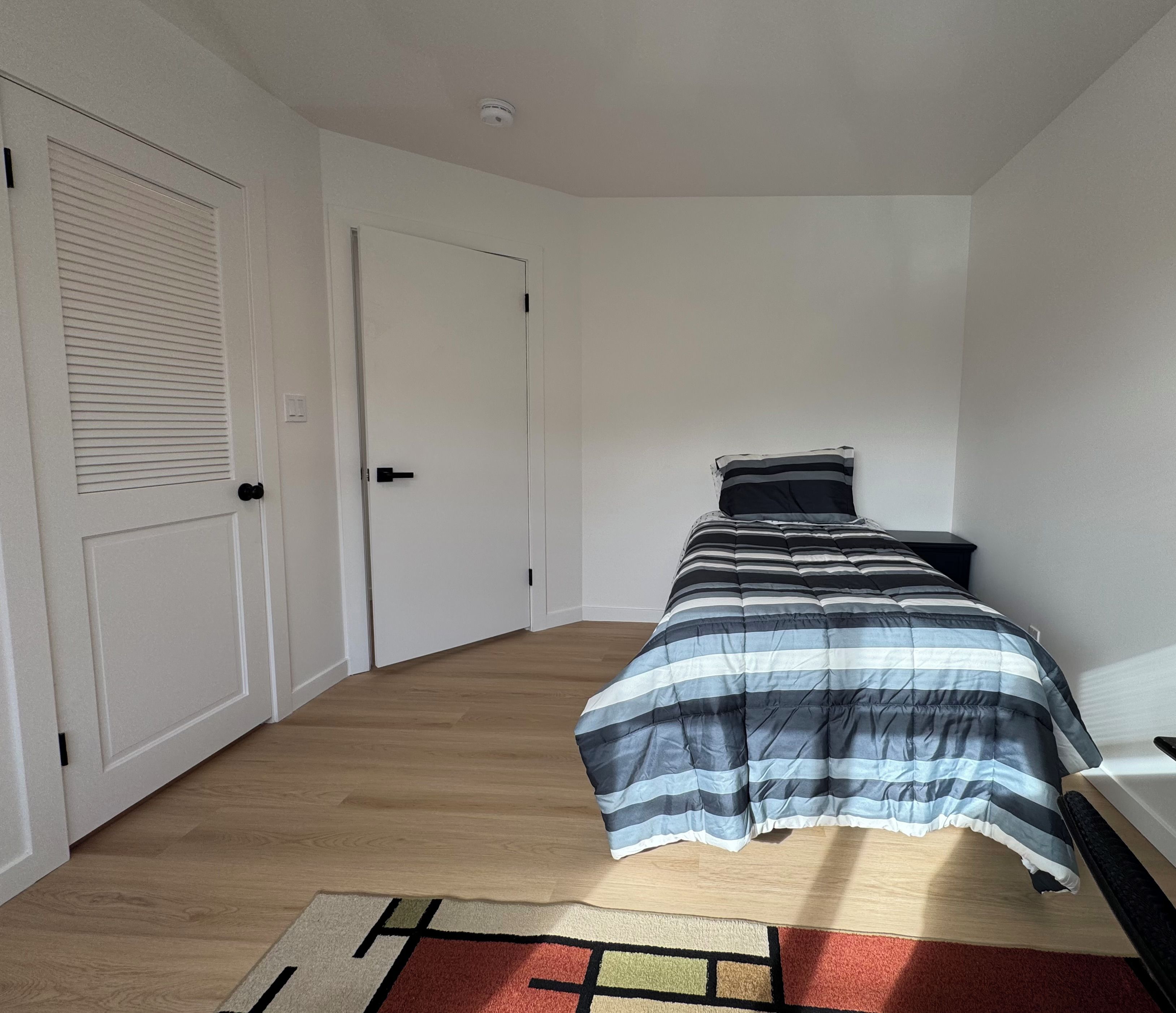 A bedroom with a bed, a nightstand, a door, and a window.