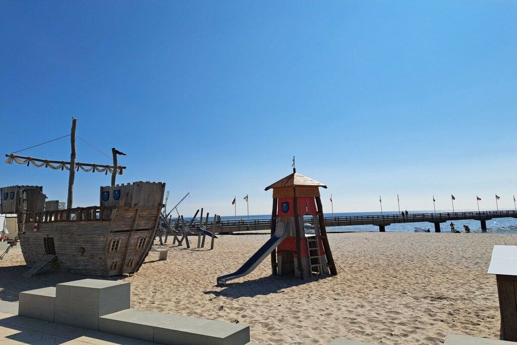 Una playa con una torre de salvavidas, una estructura de barco de madera y un muelle que se extiende hacia el agua.