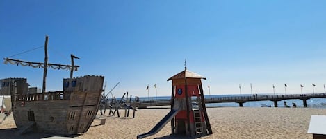 Una playa con una torre de salvavidas, una estructura de barco de madera y un muelle que se extiende hacia el agua.
