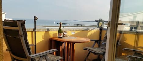 A balcony with a wooden table, two chairs, a bottle of champagne, and a glass.