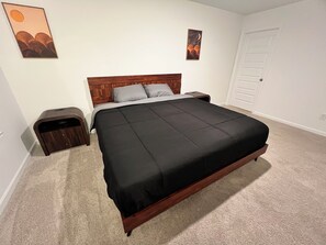 A bedroom with a wooden bed, a nightstand, a door, and two wall art pieces. - Hidden Atlanta Oasis (Atlanta)