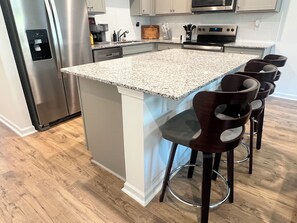 A kitchen with a granite countertop island, stainless steel appliances, and bar stools. - Hidden Atlanta Oasis (Atlanta)