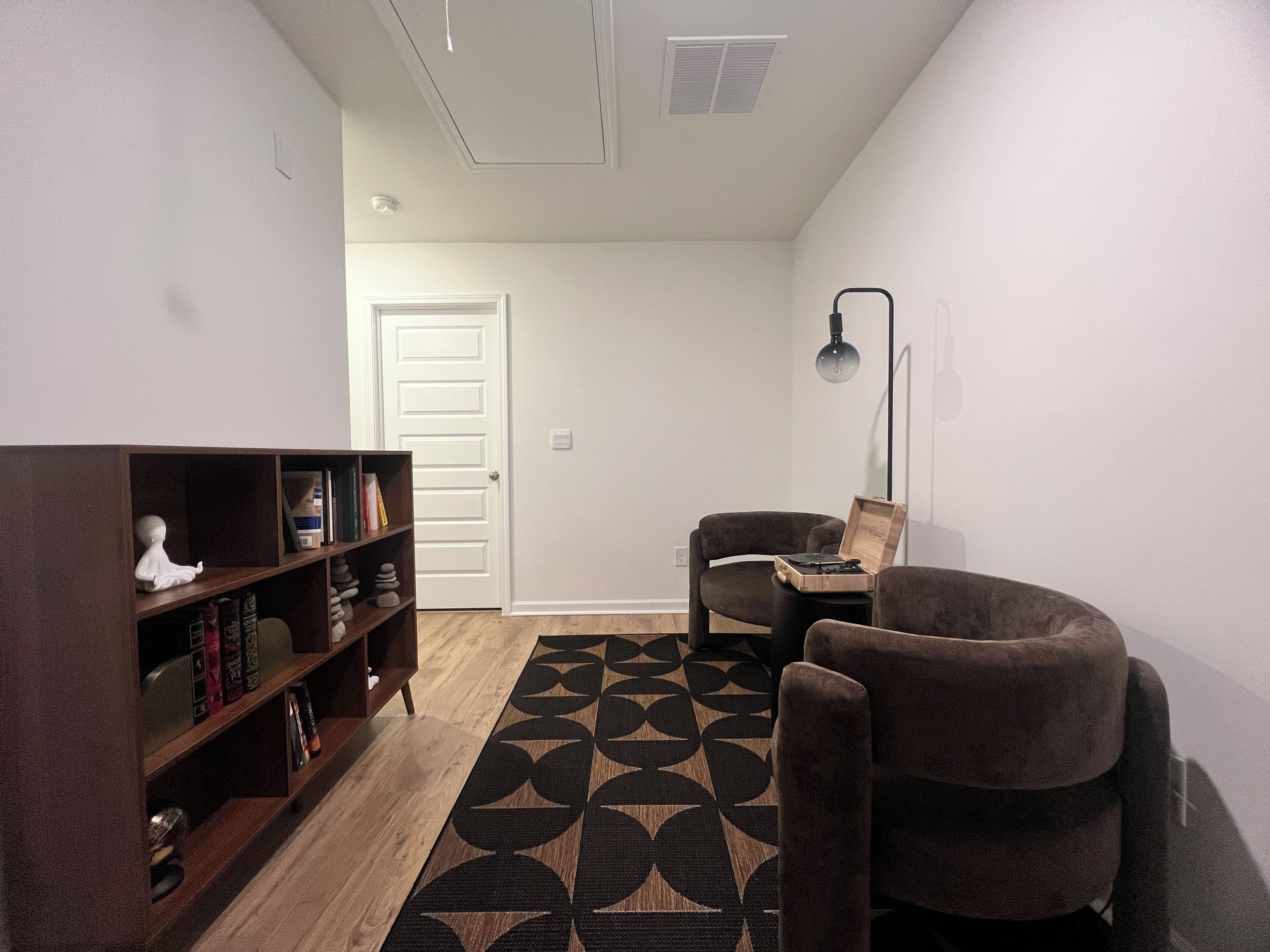 A room with a bookshelf, two chairs, a patterned rug, and a door.