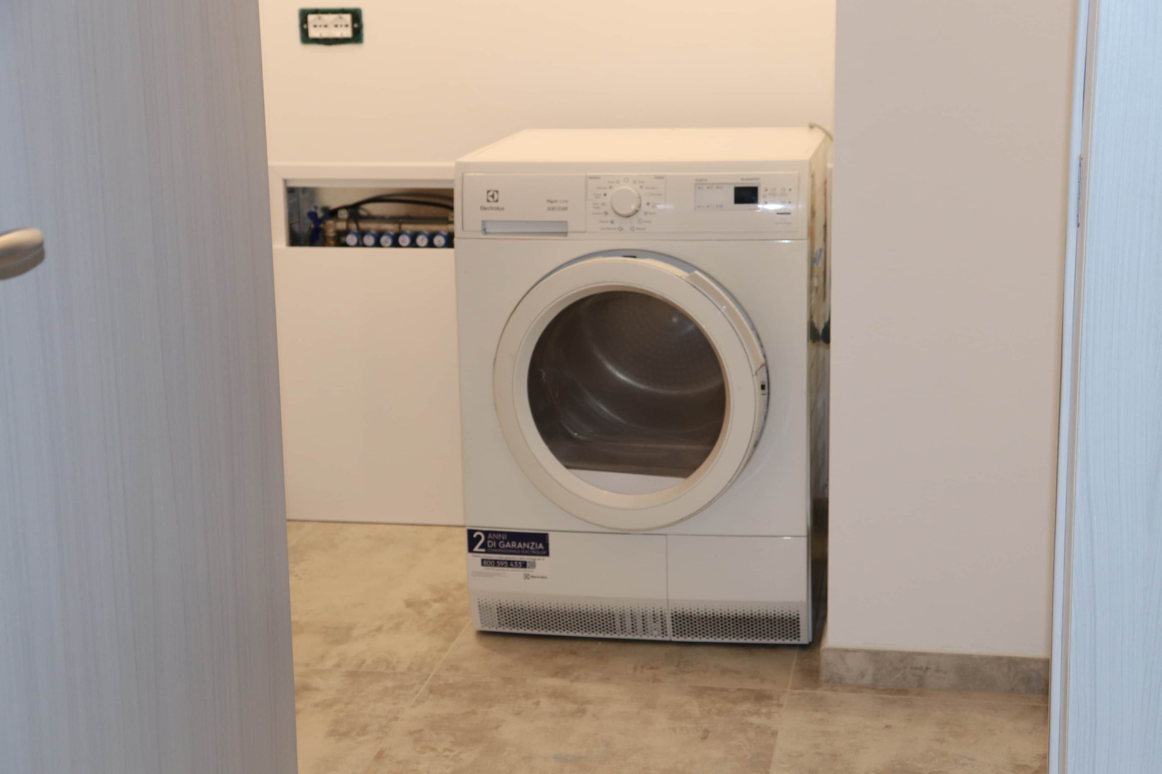 A compact, white front-loading washing machine in a small laundry room with a tiled floor.