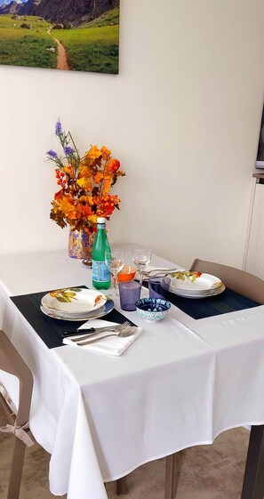 Een eettafel gedekt met borden, bestek en een decoratieve vaas met bloemen.