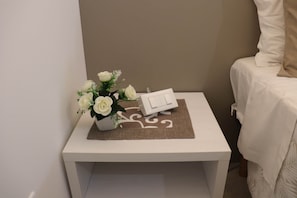 Ein kleiner Nachttisch mit einem weißen Nachtlicht und einer weißen Blumenkomposition.
