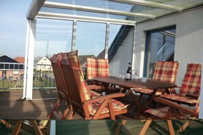 A covered patio area with a table and chairs, large windows, and a view of the surrounding area. - maritime house semi-detached house Wismar (Wohlenberg)