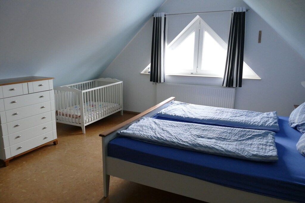 A bedroom with a single bed, a crib, a dresser, and a window with curtains.