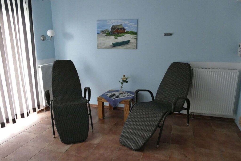 A room with two chairs, a small table with a vase, and a painting on the wall.