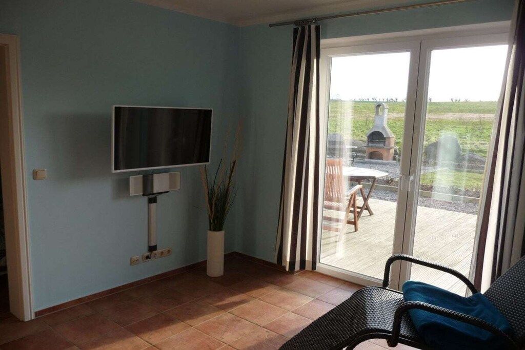 A room with a television mounted on the wall, a potted plant, a sliding glass door leading to an outdoor area with a barbecue grill, and a chair.