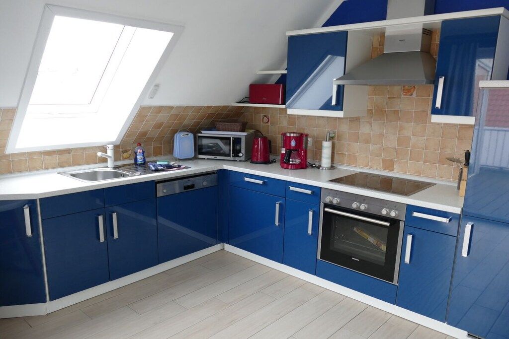A modern kitchen with blue cabinets, a microwave, a red coffee maker, and a dishwasher.