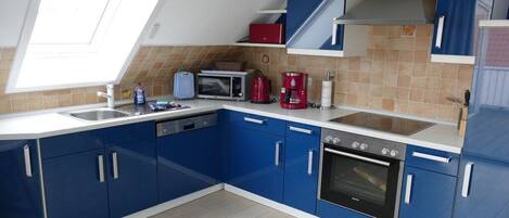 A modern kitchen with blue cabinets, a microwave, a red coffee maker, and a dishwasher.