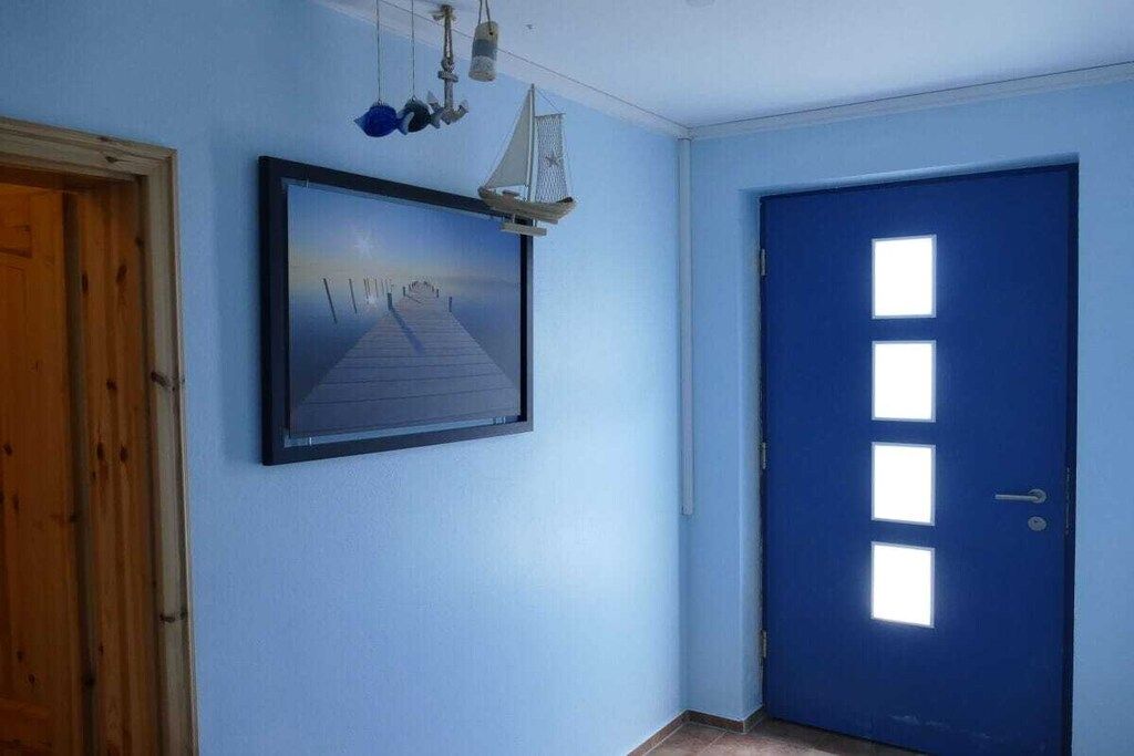 Ein Flur mit einer blauen Tür, einem gerahmten Bild an der Wand und einer Holztür links.