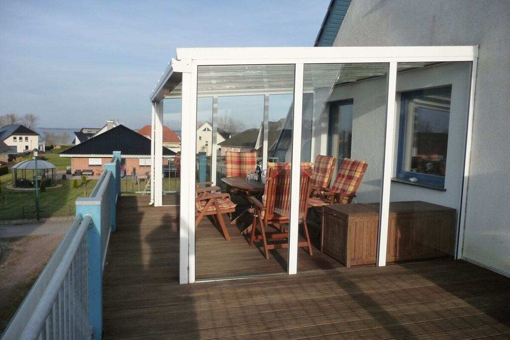 Een overdekt terras met houten meubels en een glazen constructie.
