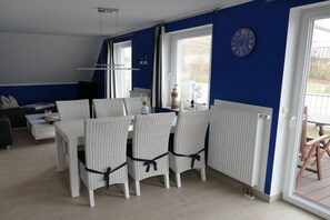 A dining area with a white table and chairs, a clock on the wall, and a view through the window. - maritime house semi-detached house Wismar (Wohlenberg)