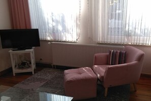 Ein Wohnzimmer mit einem Fernsehgerät auf einem weißen Schrank, einem rosa Sessel und einem Glastisch.