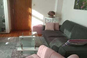Ein Wohnzimmer mit einem Glastisch, einem grauen Sofa und einem pinken Ottomanen.