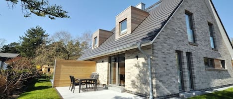 A modern house with a sloped roof, a patio with outdoor furniture, and a well-maintained lawn.