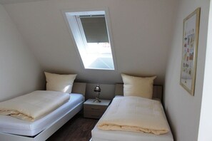 Ein Schlafzimmer mit zwei Betten, einem Nachttisch, einer Lampe und einem Fenster.