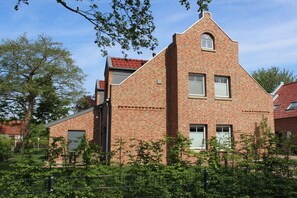 Ein Backsteinhaus mit Satteldach, einer kleinen angebauten Garage und einem umzäunten Garten mit Bäumen.