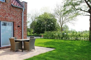 Eine Terrasse mit Tisch und Stühlen, eine Ziegelwand und ein gepflegter Rasen.