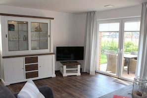 Ein Wohnzimmer mit Fernseher, einer Schrank mit Glastüren und einer Schiebetür zum Außenbereich.