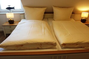 Ein Doppelbett mit zwei Nachttischen, jeweils mit einer Lampe, in einem Zimmer mit Fenster und Heizkörper.