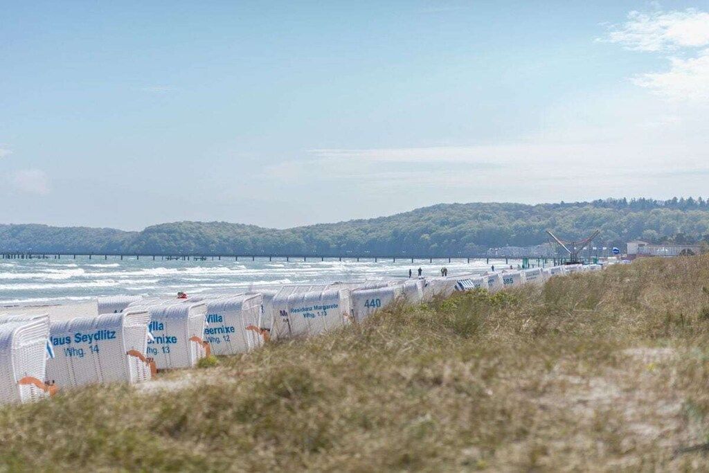 A coastal view with a beach, a pier, and a line of beach huts labeled with names and numbers.