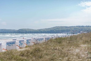 Une vue sur la côte, avec une plage, une jetée et une rangée de cabanes de plage portant des noms et des numéros.