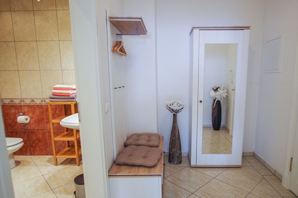 Un baño con inodoro, lavamanos, estante con toallas dobladas, un espejo y una puerta.