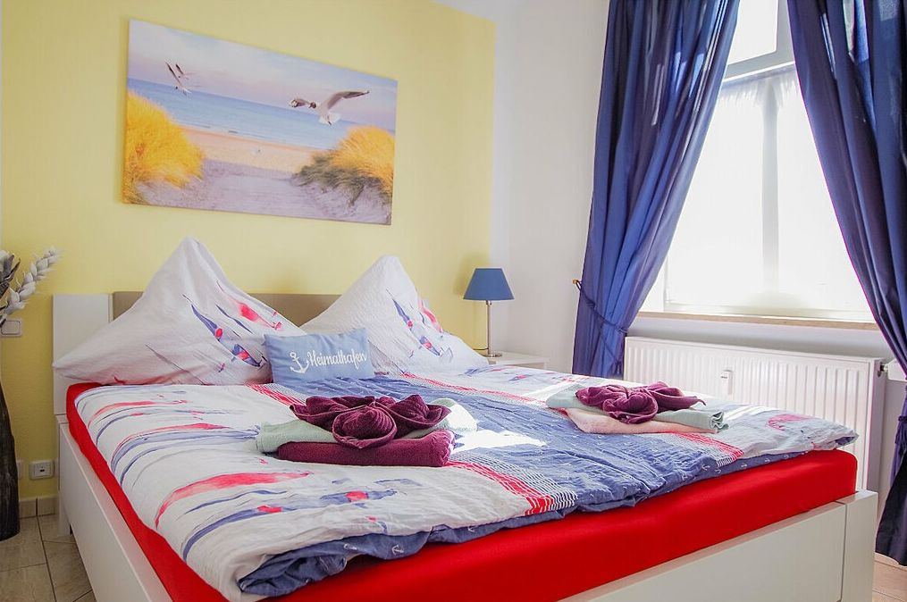 A bed with a red mattress, white headboard, and a painting of birds on the wall.