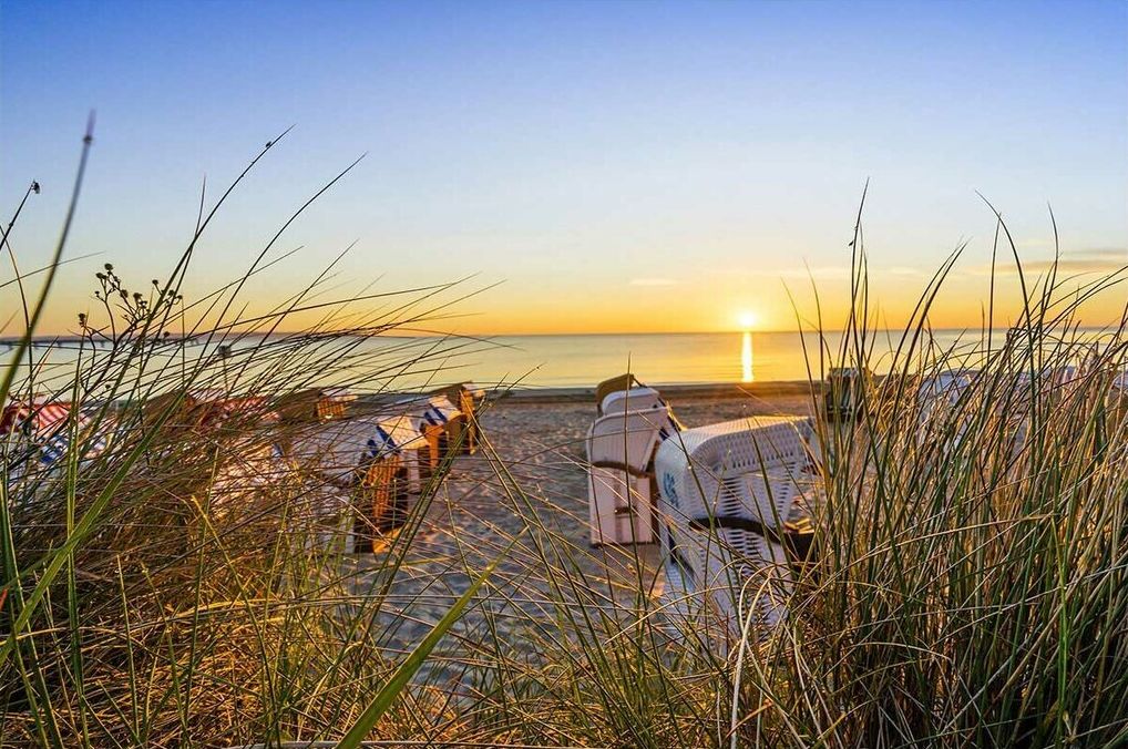 Escena de playa con atardecer, una silla y una sombrilla.