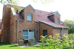 A two-story brick house with a red-tiled roof, a covered patio with outdoor furniture, and a small garden area. - Holiday home with 2 bedrooms (Greetsiel)