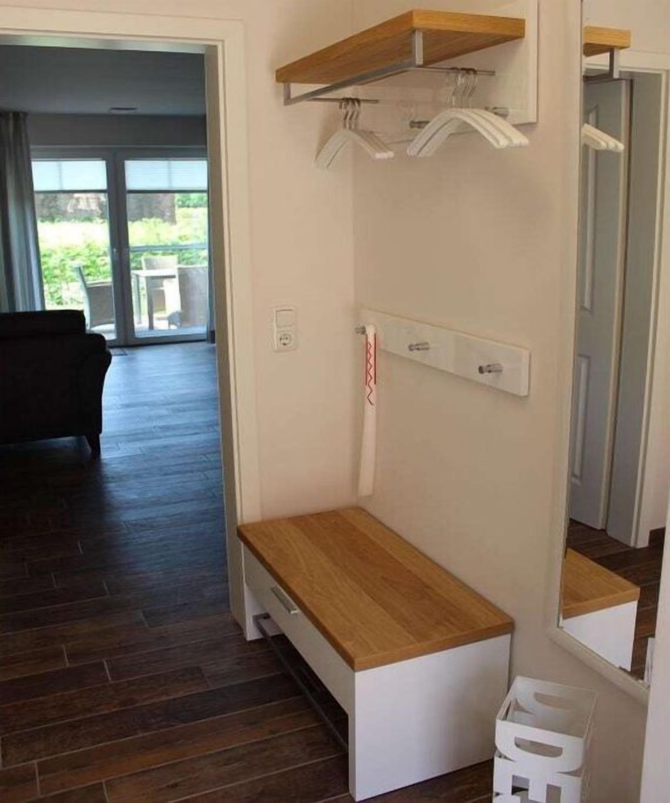 A room with a wooden bench, a white wall-mounted shelf, and a mirror.