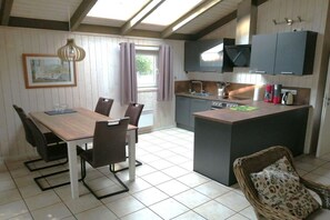 Eine kompakte Küche mit einer zentralen Kochinsel, einem Essbereich mit Tisch und Stühlen sowie ein Korbstuhl.